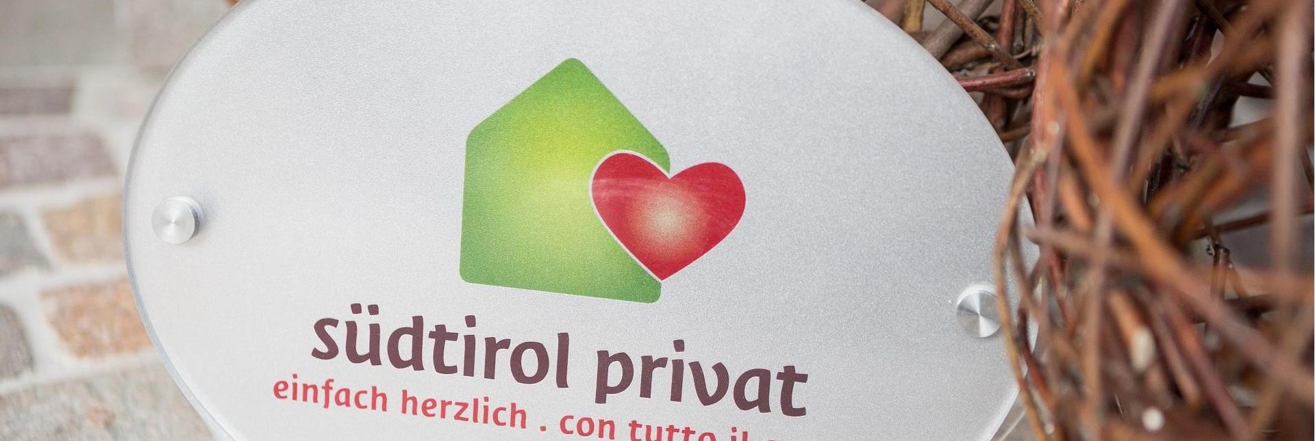 Una targhetta con il logo degli affittacamere privati e la scritta südtirol privat. einfach herzlich. con tutto il cuore